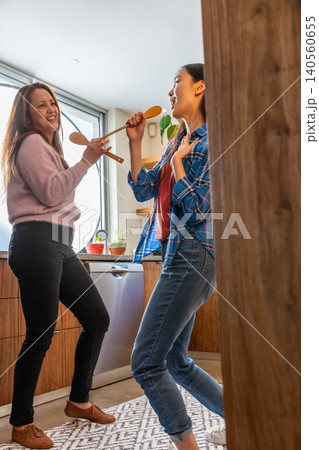 Asian mother and daughter dancing playfully in home kitchen by countertop with spoons Asian mother and daughter dancing playfully in home kitchen by countertop with spoons 140560655