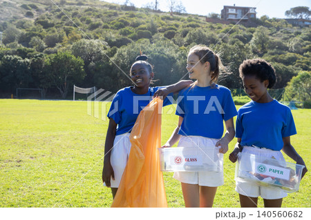Diverse teenage girls sorting recyclables on sports field using trash bag and labeled bins 140560682