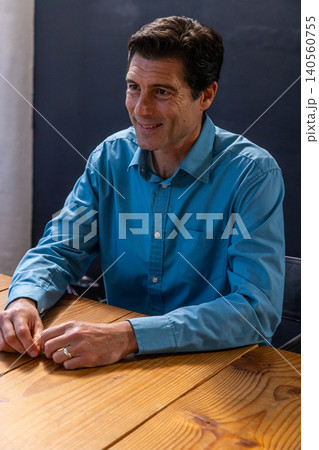 Middle-aged man leaning forward at wooden meeting table in conference room 140560755