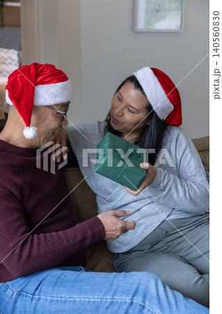 Asian family exchanging green wrapped gift on living room sofa in santa hats Asian family exchanging green wrapped gift on living room sofa in santa hats 140560830