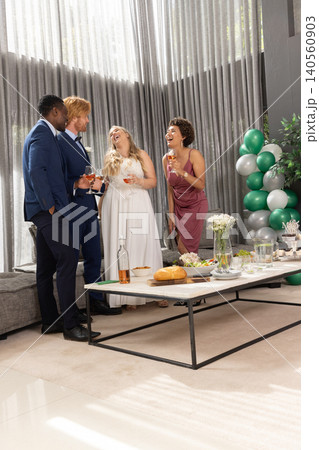 Wedding group in formal wear raising rosé glasses at table in reception lounge 140560903