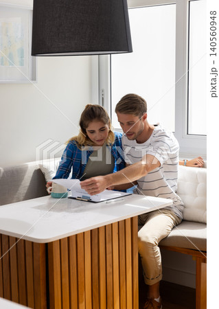 Couple reviewing papers on clipboard while sitting at wooden table in dining nook with coffee mug Couple reviewing papers on clipboard while sitting at wooden table in dining nook with coffee mug 140560948