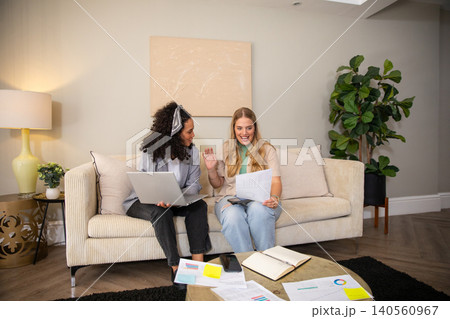 Diverse female coworkers reviewing charts, using laptop on coffee table in home office lounge Diverse female coworkers reviewing charts, using laptop on coffee table in home office lounge 140560967