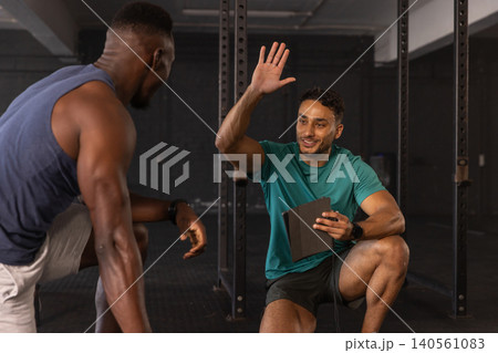 Middle eastern trainer high fiving african american client by squat rack using tablet Middle eastern trainer high fiving african american client by squat rack using tablet 140561083