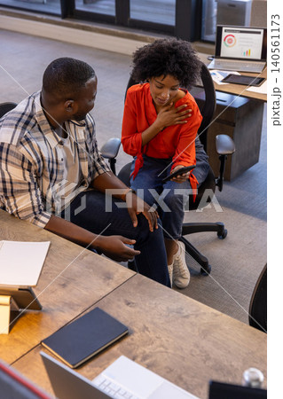 African american colleagues leaning at wooden desk in office holding smartphone African american colleagues leaning at wooden desk in office holding smartphone 140561173