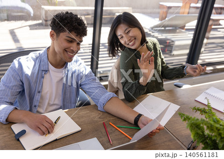 Diverse coworkers reviewing printed chart in office at table with laptop, notebooks and potted fern 140561181