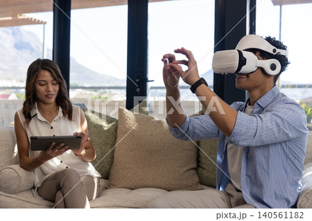 Diverse friends sitting on sofa in living room using tablet and vr headset, copy space Diverse friends sitting on sofa in living room using tablet and vr headset, copy space 140561182