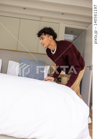 Hispanic male wearing sweater and trousers making king-size bed in bedroom, copy space Hispanic male wearing sweater and trousers making king-size bed in bedroom, copy space 140561197
