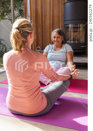 Diverse female yoga partners practicing meditation at home on rose and purple mats Diverse female yoga partners practicing meditation at home on rose and purple mats 140561274