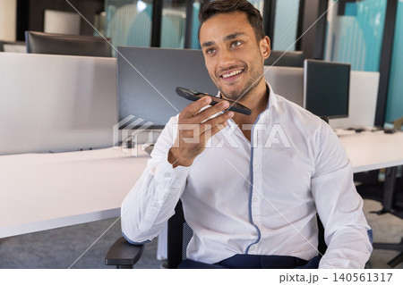 South asian man in dress shirt sitting at office desk with smartphone speakerphone, copy space 140561317