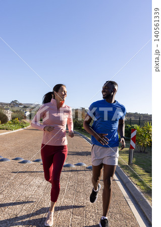 Couple jogging in athletic wear together along suburban path past striped marker under sky Couple jogging in athletic wear together along suburban path past striped marker under sky 140561339