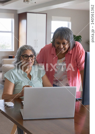Senior Asian women friends sitting at table interacting with laptop and mouse in home workspace Senior Asian women friends sitting at table interacting with laptop and mouse in home workspace 140561362