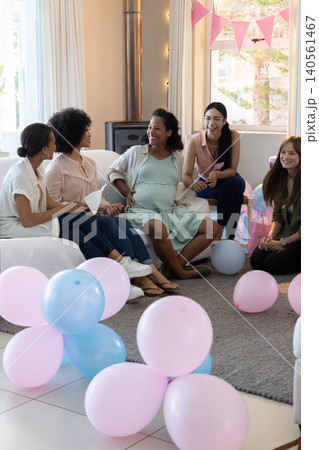 Diverse female friends celebrating baby shower in living room with balloons, bunting Diverse female friends celebrating baby shower in living room with balloons, bunting 140561467