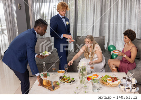 Diverse newlywed couple with friends reaching for appetizers on coffee table in living room 140561512