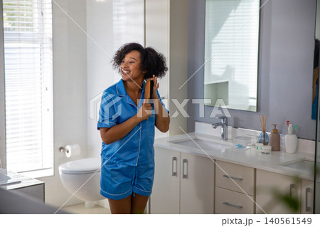 African american woman wearing blue pajamas brushing curly hair, wooden brush beside dual sink 140561549