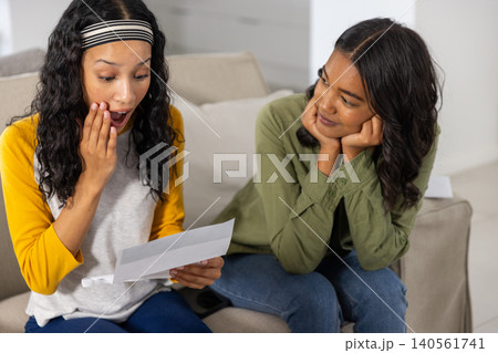 Diverse mom and teenage daughter sitting side by side on beige sofa in living room 140561741