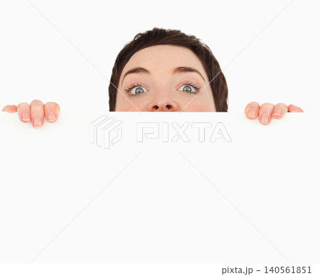 Woman peeking over large white panel in studio, gripping edge with manicured nails 140561851