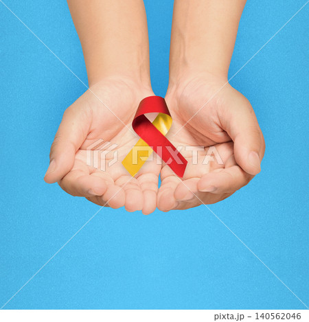 Hands cupped together holding a red and yellow awareness ribbon against a blue background, symbolizing support for Hepatitis C Hands cupped together holding a red and yellow awareness ribbon against a blue background, symbolizing support for Hepatitis C 140562046