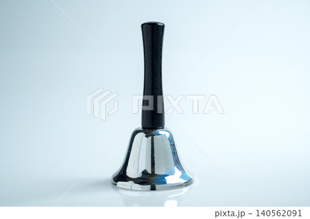 A close-up studio shot of a polished metallic silver handbell featuring a sleek black handle, set against a clean, bright, and neutral white background 140562091