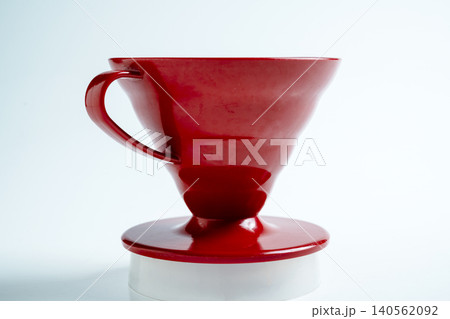 A close-up shot of a bright red ceramic pour-over coffee dripper cone with a handle, sitting on a white background, perfect for manual filter brewing A close-up shot of a bright red ceramic pour-over coffee dripper cone with a handle, sitting on a white background, perfect for manual filter brewing 140562092