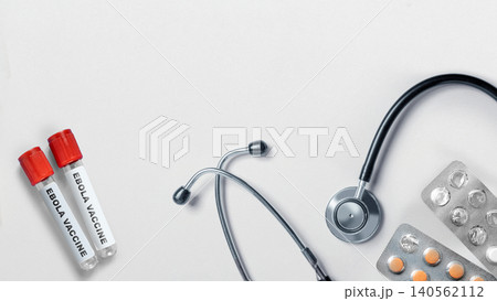 High-angle view of two vials labeled Ebola Vaccine, a stethoscope, and blister packs of pills, symbolizing medical research, disease prevention, and public health initiatives 140562112