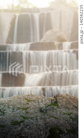 Natural mossy rock foreground serves as an empty product display pedestal against a beautiful, softly blurred multi-tiered waterfall background with warm light Natural mossy rock foreground serves as an empty product display pedestal against a beautiful, softly blurred multi-tiered waterfall background with warm light 140562235