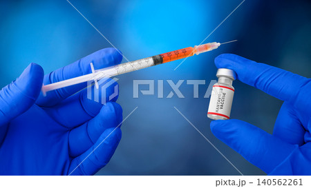 A medical professional in blue gloves holds a syringe filled with orange liquid next to a Hantavirus vaccine vial 140562261