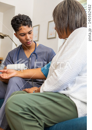 Asian male nurse in gray scrubs and senior patient measuring blood pressure with cuff on couch Asian male nurse in gray scrubs and senior patient measuring blood pressure with cuff on couch 140562482