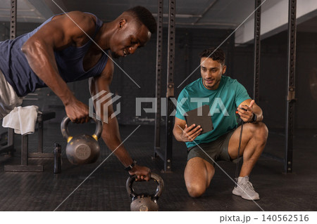 Diverse coach and client training with kettlebells in gym weight area using tablet and stopwatch Diverse coach and client training with kettlebells in gym weight area using tablet and stopwatch 140562516
