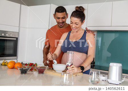 Diverse couple mixing berries in glass blender jar at modern kitchen island with colorful bowls Diverse couple mixing berries in glass blender jar at modern kitchen island with colorful bowls 140562611
