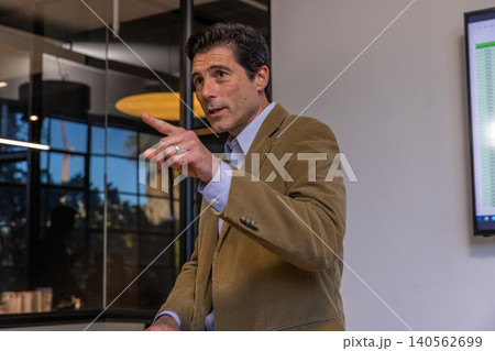 Man gesturing and presenting spreadsheet by glass wall in boardroom under circular light 140562699