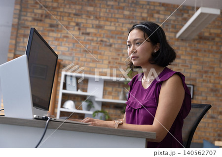 Asian woman working at desk on computer monitor in office, copy space Asian woman working at desk on computer monitor in office, copy space 140562707