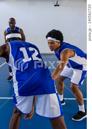 African american male teammates performing defensive drill on gym with basketball by hoop 140562720
