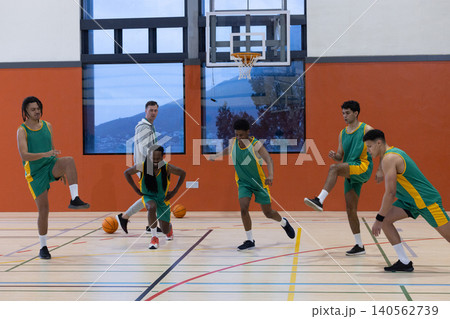 Basketball coach along with five players in green jerseys performing lunges under hoop 140562739