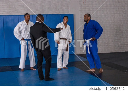 Diverse male group practicing martial arts techniques in gis, belts on dojo mats with instructor Diverse male group practicing martial arts techniques in gis, belts on dojo mats with instructor 140562742