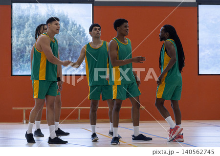 Diverse male teammates wearing green and yellow jerseys shaking hands, chatting on basketball court 140562745