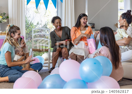 Expectant mother opening gift bag in living room surrounded by pastel balloons 140562817