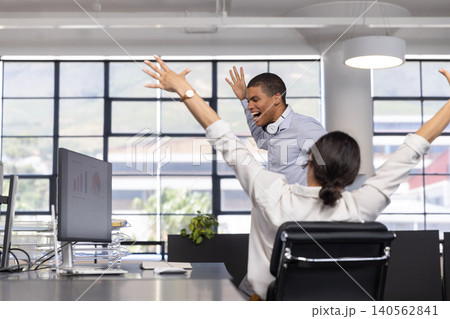 African american male coworkers celebrating success at office desks with computer charts African american male coworkers celebrating success at office desks with computer charts 140562841