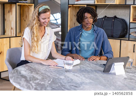Diverse coworkers flipping through printed documents and referencing tablet at office meeting table 140562858