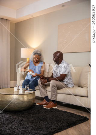 Senior couple sitting on beige sofa at home dispensing pills from white bottle over coffee table Senior couple sitting on beige sofa at home dispensing pills from white bottle over coffee table 140562917