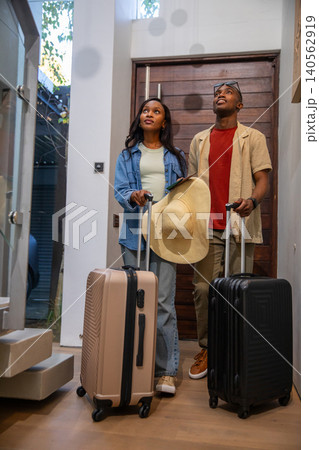 African American couple standing at home entryway holding suitcases and hat looking upward African American couple standing at home entryway holding suitcases and hat looking upward 140562919