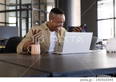 African american man checking smartphone in modern office, using laptop, vr headset African american man checking smartphone in modern office, using laptop, vr headset 140563044