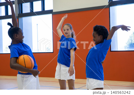 Diverse female teammates raising arms and holding basketball in sportswear on gym court 140563242