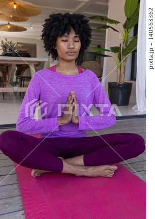 African american woman meditating in purple athletic wear on yoga mat on covered wooden deck African american woman meditating in purple athletic wear on yoga mat on covered wooden deck 140563362