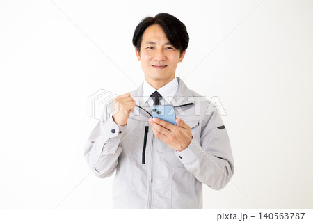 スマホを持ってガッツポーズするグレーの作業着のミドル男性ビジネスマン白バック 140563787