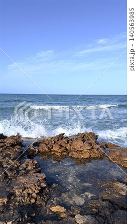 Rocky shoreline with waves breaking under clear blue sky Rocky shoreline with waves breaking under clear blue sky 140563985