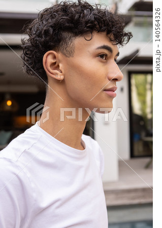 Man standing on wooden pool deck by glass doors wearing t-shirt and hoop earrings Man standing on wooden pool deck by glass doors wearing t-shirt and hoop earrings 140564326