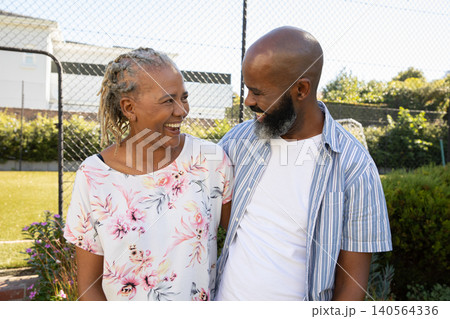 African American couple smiling with arm around shoulder while standing by chain-link fence in yard African American couple smiling with arm around shoulder while standing by chain-link fence in yard 140564336