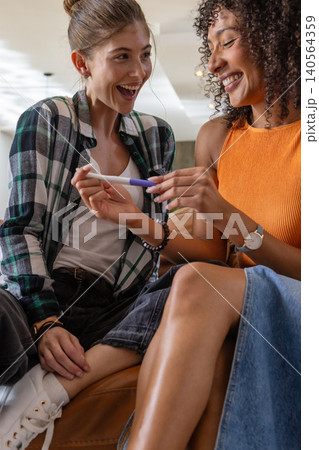 Diverse female couple examining pregnancy test while sitting on leather sofa in living room Diverse female couple examining pregnancy test while sitting on leather sofa in living room 140564359