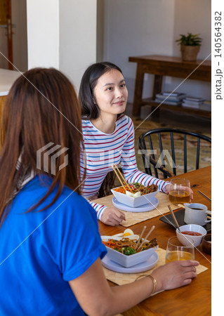Asian mother and daughter eating noodle soup with chopsticks at dining table sipping iced tea 140564382